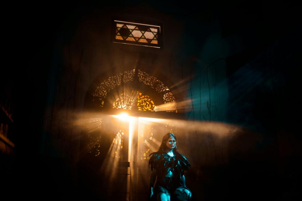 A woman in dramatic lighting poses in an atmospheric setting with rays of light.
