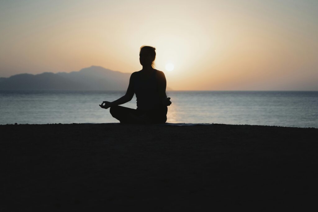 pexels-photo-5928615-5928615 A woman practices meditation with a tranquil ocean sunset backdrop, embodying peace and relaxation.