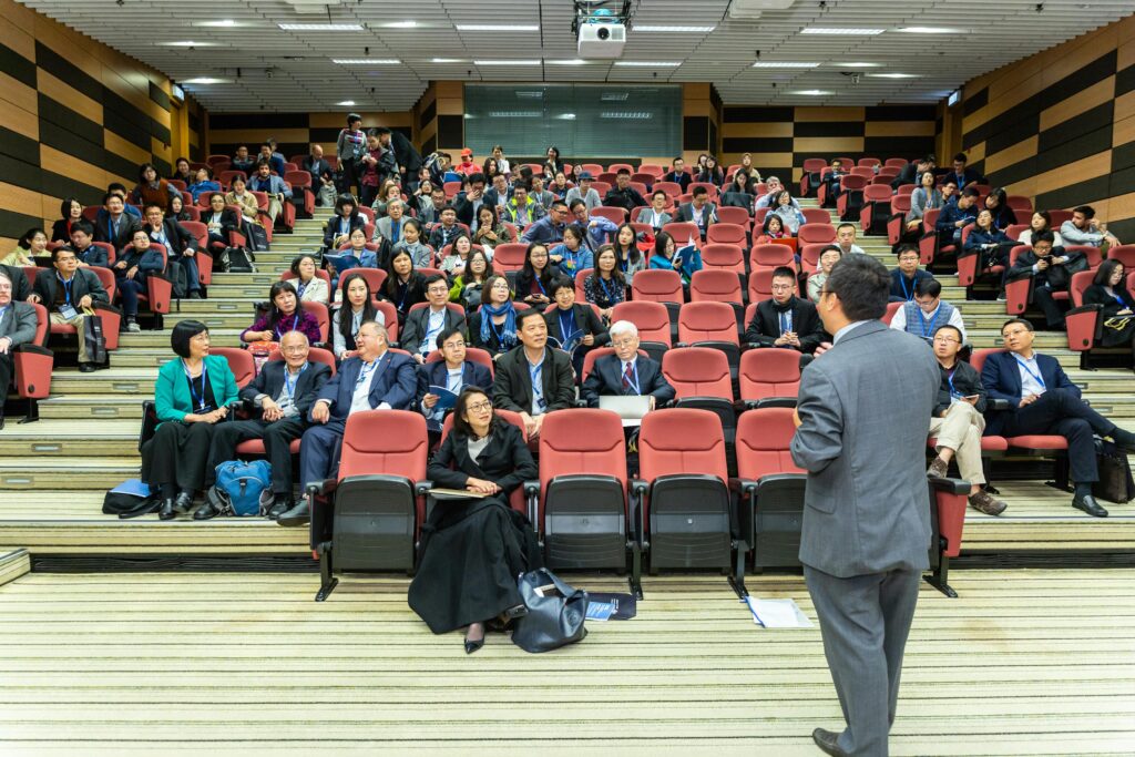 pexels-photo-1709003-1709003 Professional setting of a business conference with attendees and a presenter in an auditorium.