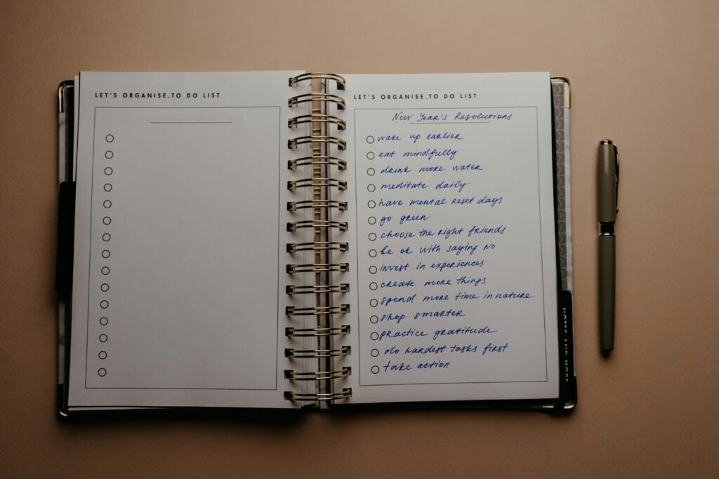 pexels-photo-5717413-5717413 Open planner with New Year's resolutions, spiral binding, and pen on warm-toned background.