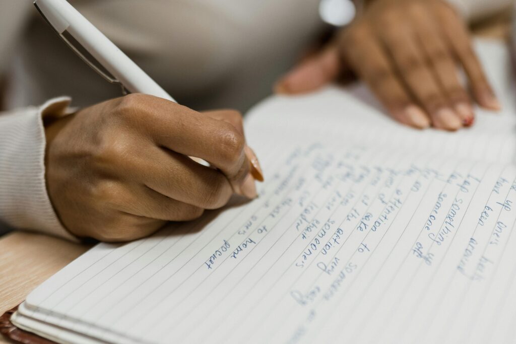 pexels-photo-6550404-6550404 Focused close-up of hands writing notes in a lined notebook with a pen.