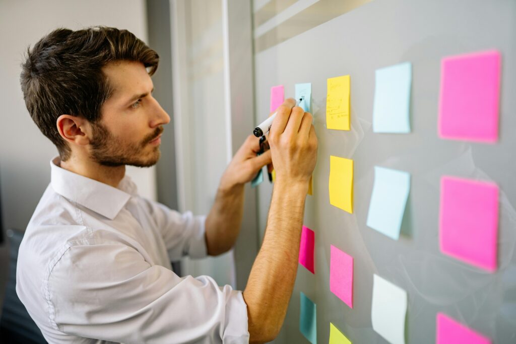 pexels-photo-7793103-7793103 Focused businessman writing on sticky notes in a modern office environment.